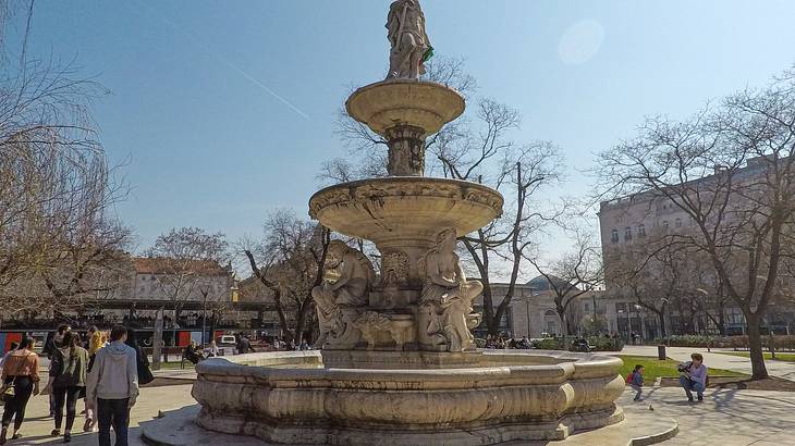 A fountain in a square next to bare winter trees under a blue sky