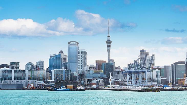 A city skyline next to the water under the clouds and blue sky