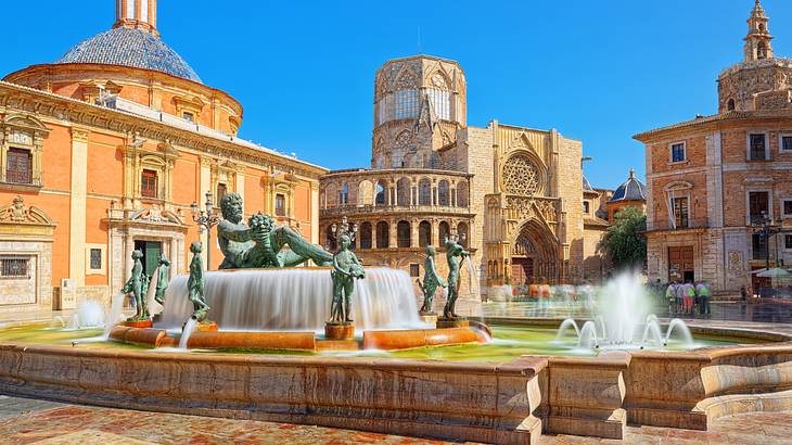 A water fountain with sculptures near old buildings on a bright day