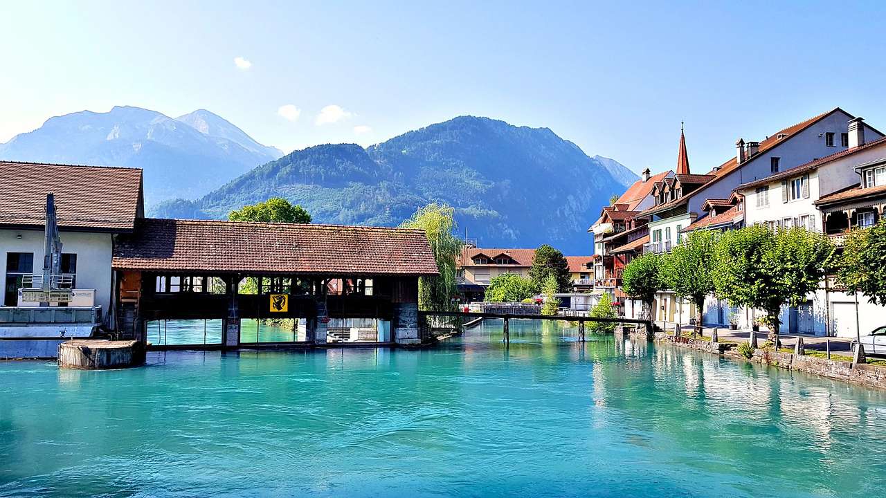 A body of water next to a covered bridge and buildings with a mountain behind