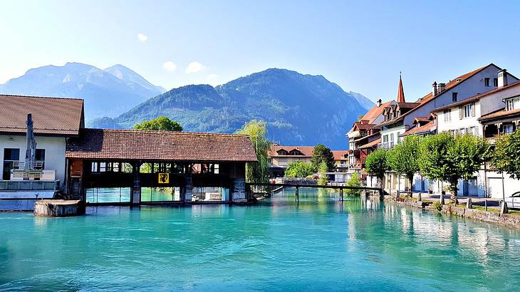 A body of water next to a covered bridge and buildings with a mountain behind