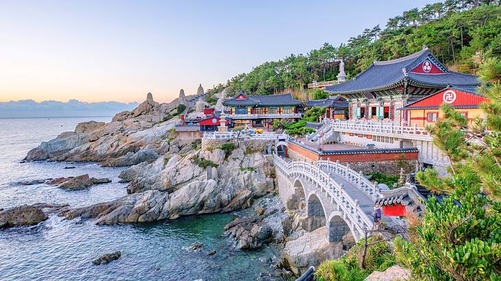 Colorful temples and a small bridge by a coastal rocky terrain near trees