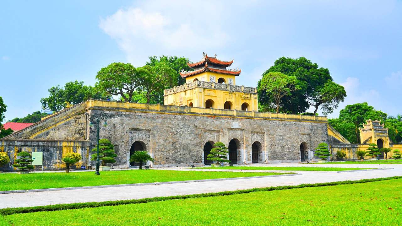 A yellow and stone temple-style structure next to green trees and green grass