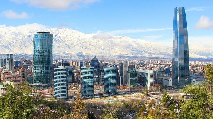 A city with tall buildings and trees and a distant view of snowcapped mountains