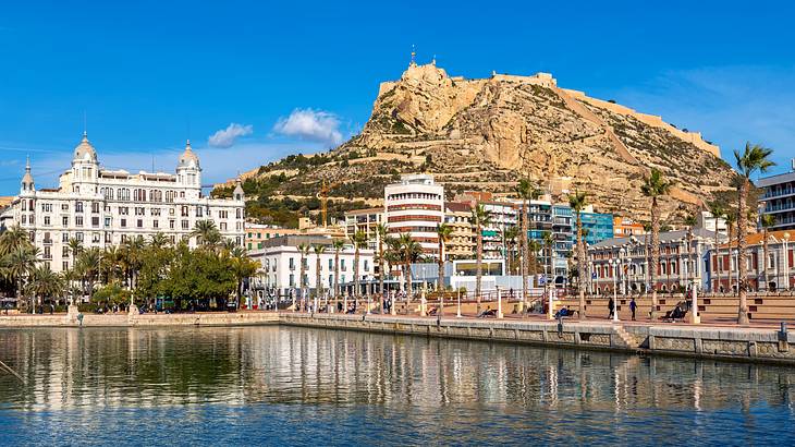 Buildings near a body of water and a mountain under a blue sky