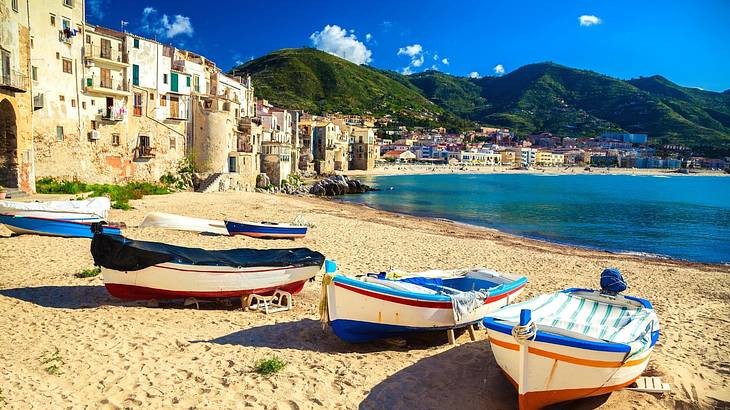 Boats sitting on the sand next to water with mountains and a town at the back
