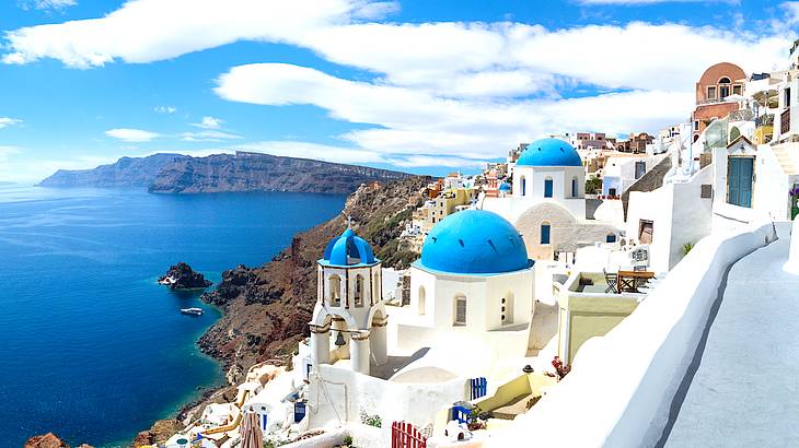 Blue domes on top of white houses overlooking an island in the distance and blue seas