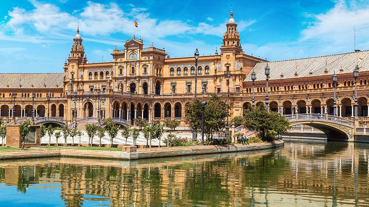 A grand historic building next to a waterfront, trees, and a bridge