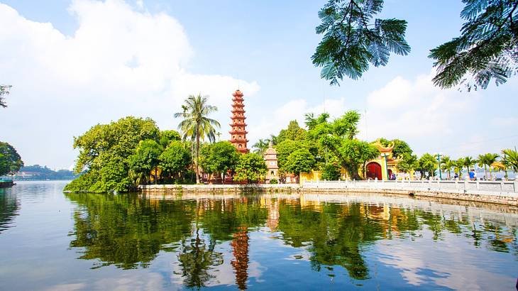 A pagoda next to trees and a lake with a reflection in it on a bright day