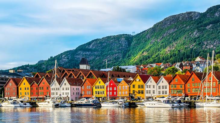 Small colourful houses next to the water with greenery-covered mountains behind them