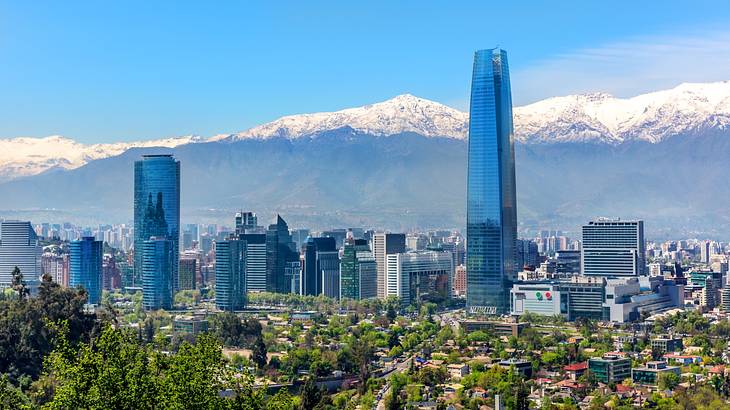 A city skyline full of tall and short buildings, trees and snow-capped mountains