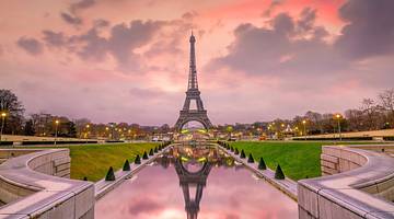 The Eiffel Tower reflected in a canal amongst gardens at sunrise