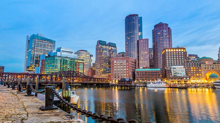 A city skyline with lit-up buildings and a bridge, from across a body of water