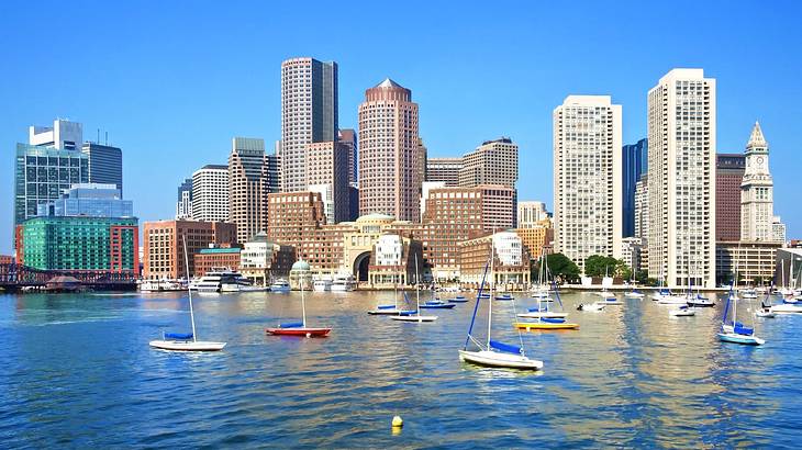 A city skyline with water and boats in front under a clear blue sky