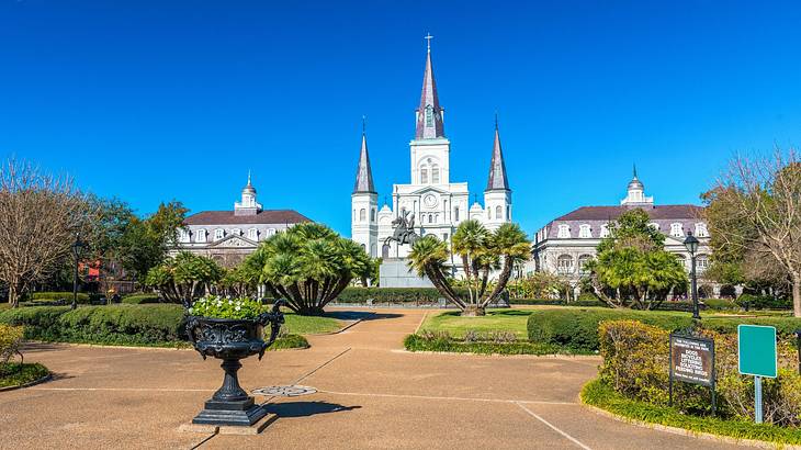 A white cathedral with three spires next to a garden with greenery and a path