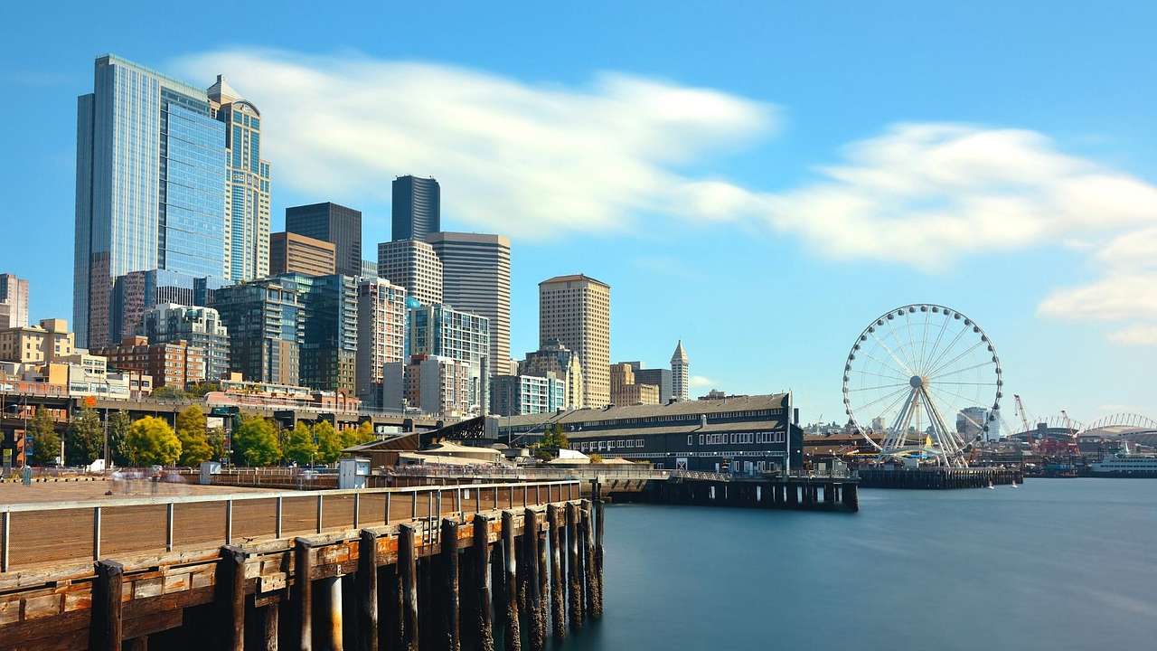 A city skyline and a Ferris wheel next to a pier and a bay of water on a clear day