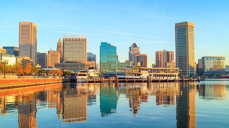 A city skyline reflecting onto the water in front of it under a blue sky