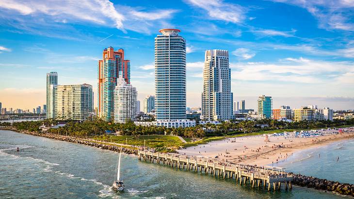 Skyscrapers surrounded by palm trees and a beach, against a partly cloudy sky