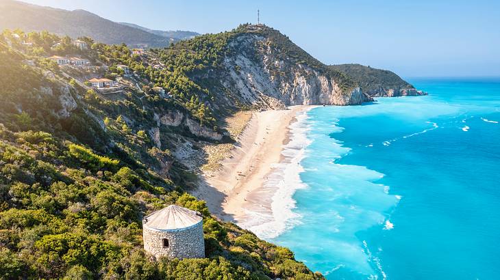 A beach surrounded by lush rocky mountains with a cylindrical structure atop