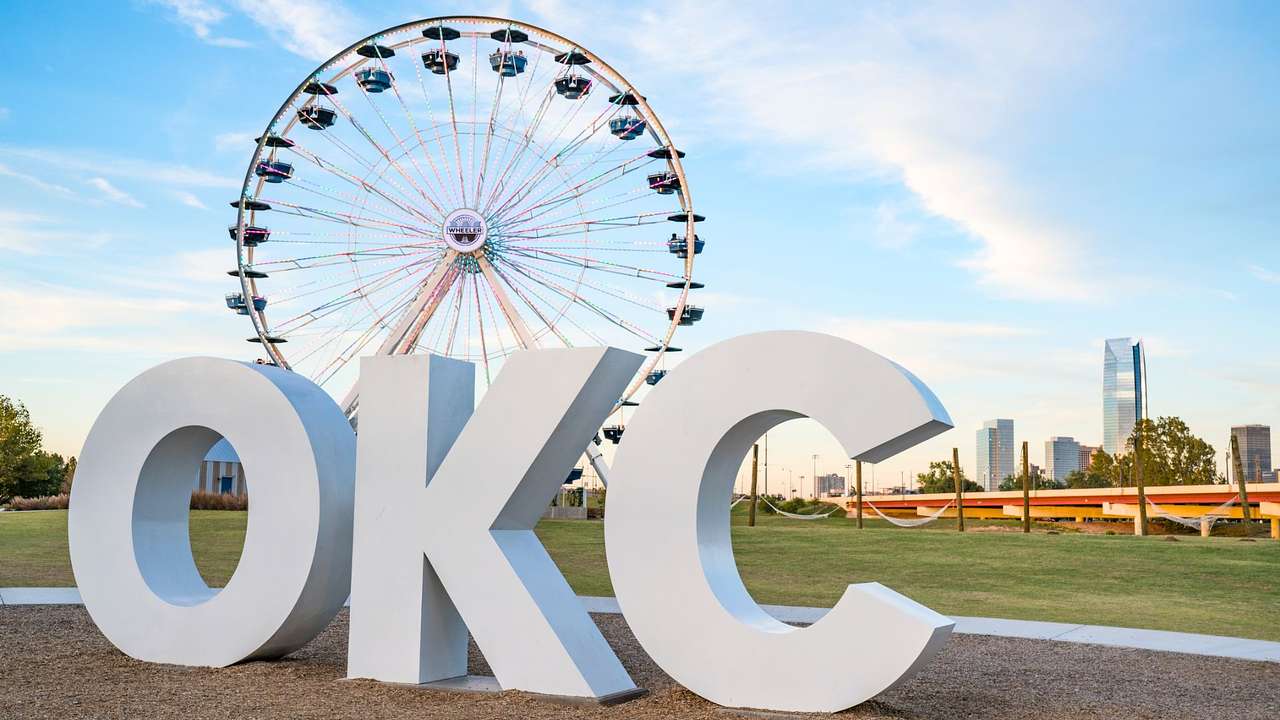 A large white sign that says "OKC" next to a Ferris wheel in a park