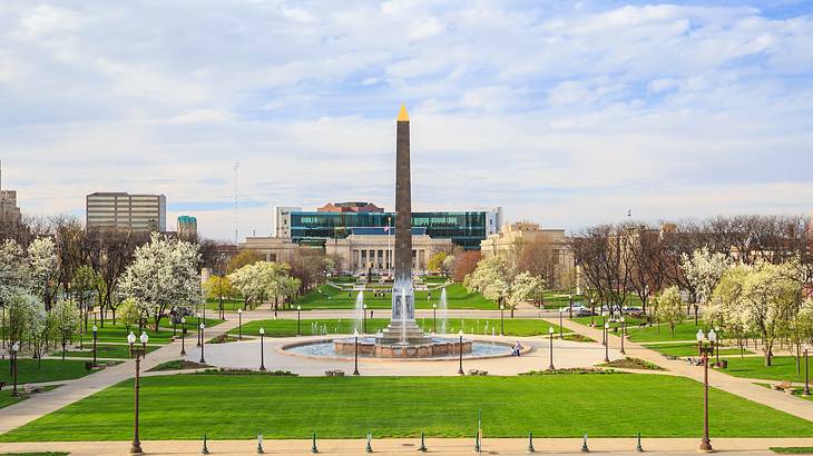 A park with a tall obelisk in the middle surrounded by paved pathways and trees