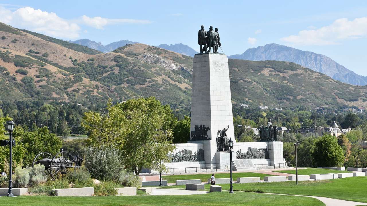 A tall monument with statues of men on the top in the middle of a park near mountains