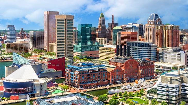 City buildings next to greenery and water under a blue sky with clouds