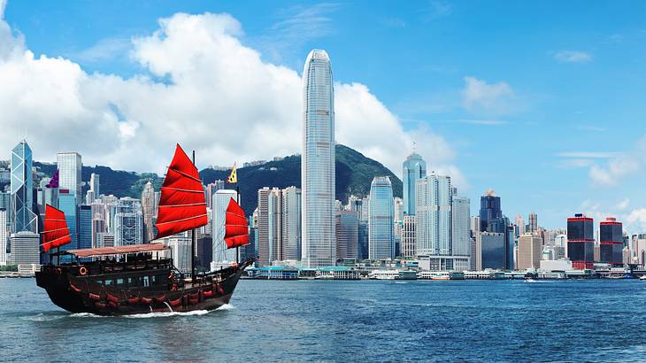 A city skyline near a body of water with a boat with red sails