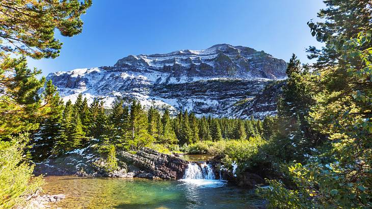 A waterfall in the middle of a forest at the foot of a snow-streaked mountain