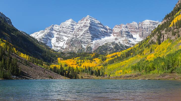 Mountain peaks with light snow and green tree-filled mountains and water in front