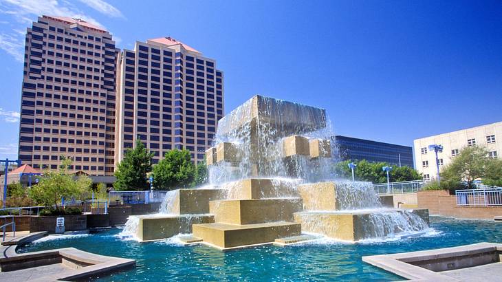 A water fountain near buildings and trees under a blue sky