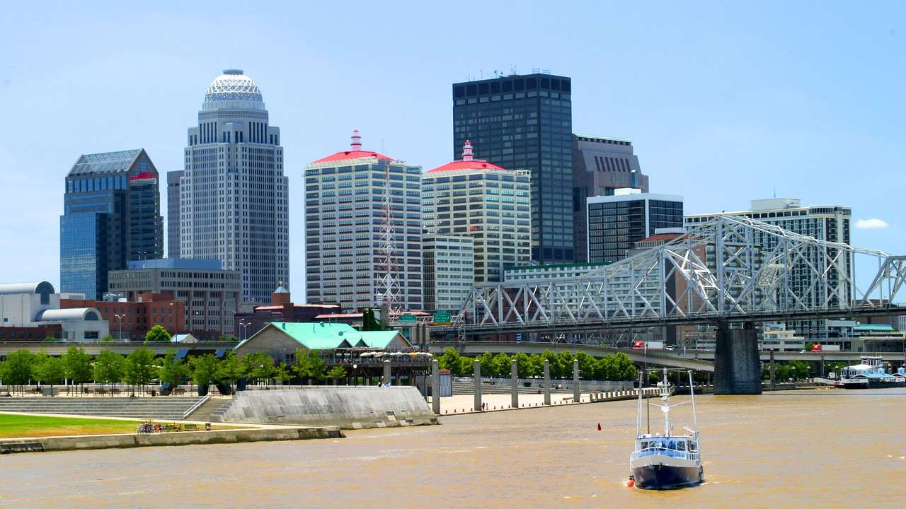 A city skyline next to a bridge over a river with a boat on it