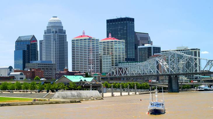 A city skyline next to a bridge over a river with a boat on it