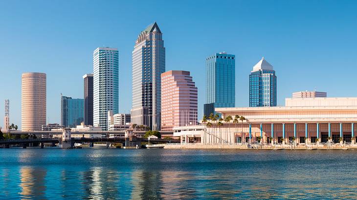 Skyscrapers and a smaller building next to a body of water under a blue sky