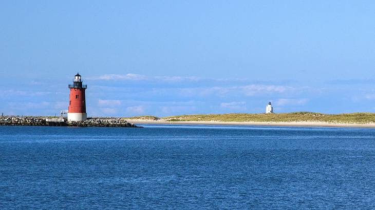 Blue water with a red and white lighthouse next to greenery and another lighthouse