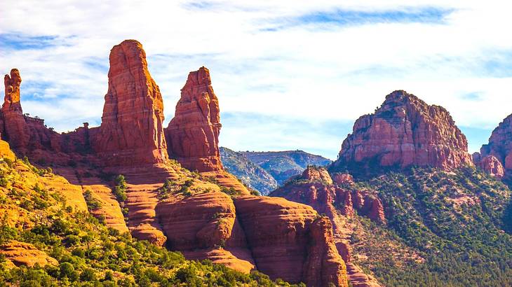 A hill with sandstone towers and red rock formations under a partly cloudy sky