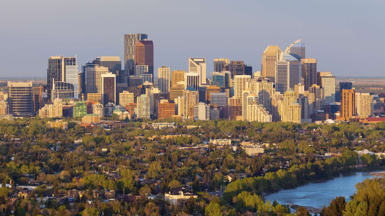 A city skyline from far away with trees and a lake in front of it, on a clear day