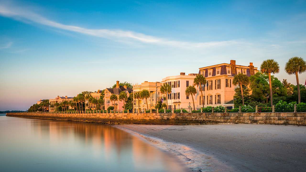 Buildings with trees facing a calm ocean during sunset, under a clear blue sky