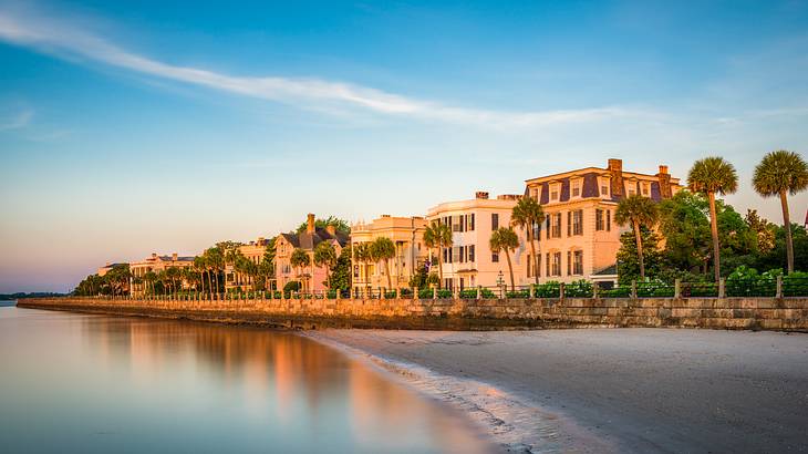 Buildings with trees facing a calm ocean during sunset, under a clear blue sky