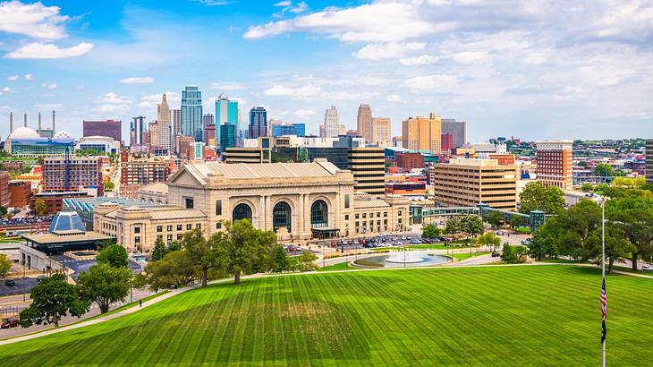 A view of a city with green grass in the foreground under a blue sky with clouds