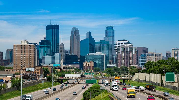 Multi-lane freeways with a city skyline in the background under a blue sky