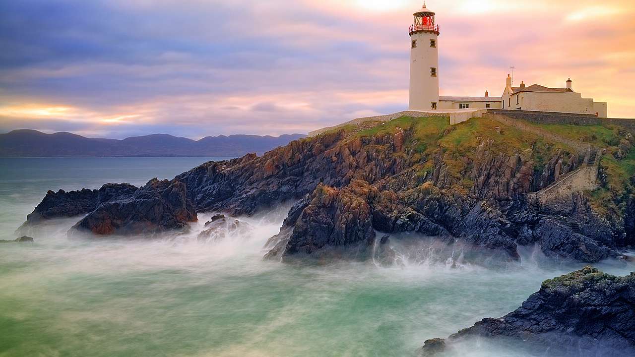 Waves breaking on a rocky shore with a lighthouse on top and an overcast sky