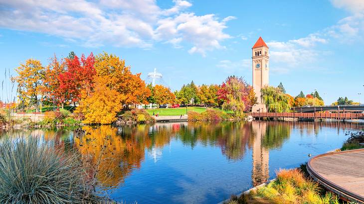 A lake near a clock tower and red, orange, and green trees during the fall