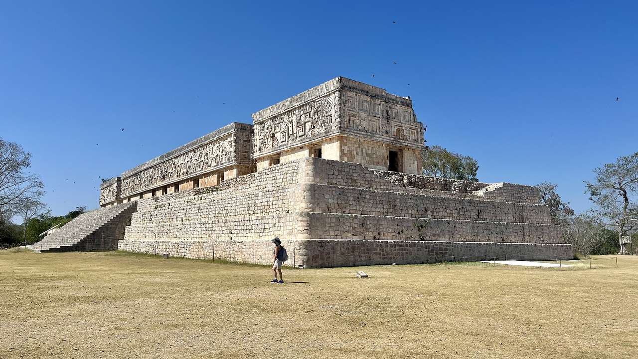 Rectangular ancient Mayan ruins with a person and dry grass around on a clear day