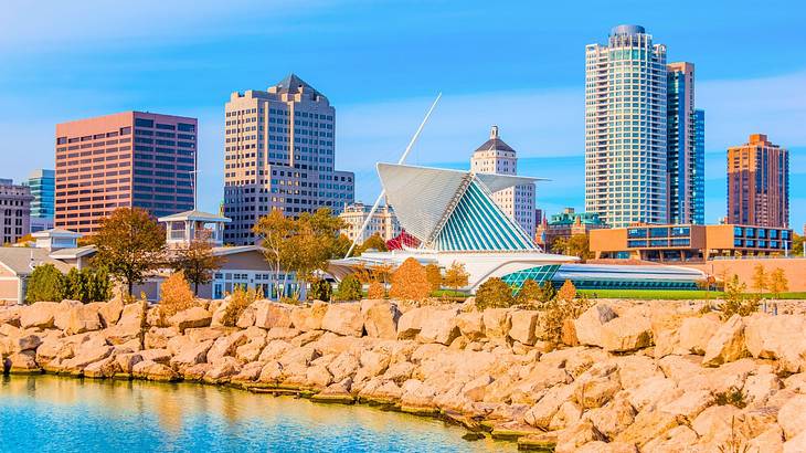 A modern structure and tall buildings near a rock wall and the water