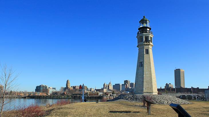 A lighthouse with a city skyline and a bright blue sky in the background