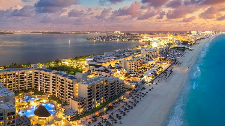 A long stretch of beach with numerous resorts along the waterfront lit up at sunset