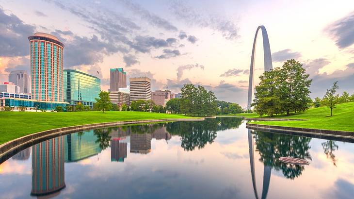 A huge arch monument facing a skyline, overlooking a pond winding through green grass