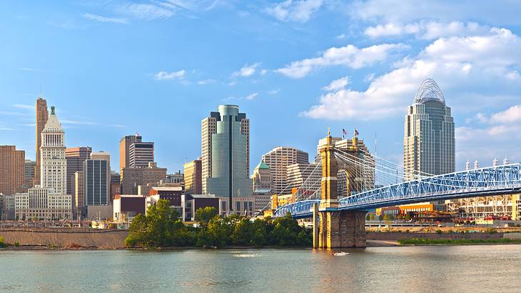 A river with a bridge over it next to a city skyline under a blue sky with clouds