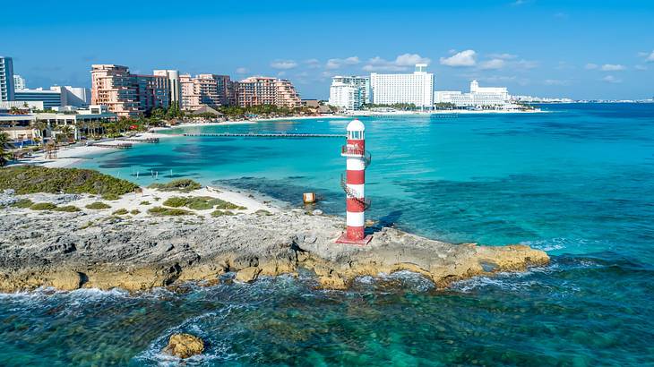 A rocky beach with a red and white pole and buildings next to the ocean